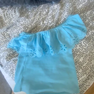 Ljusblå offshoulder topp från Zara - Säljer en söt ljusblå offshoulder topp från Zara med volangdetaljer och broderade blommor. Perfekt för sommardagar och ger en fräsch look. Passar både till jeans och kjol. 🌸knappt använd och inga defekter❤️från Zaras barnavdelning storlek 13-14 år/164 men passar mig som brukar ha mellan xxs-s