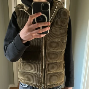  Manchester dunväst från Stenströms - Snygg väst från Stenströms med dragkedja och huva. Västen har en broderad detalj och är perfekt för kyligare dagar. Den har en quiltad design som ger extra värme och stil. 