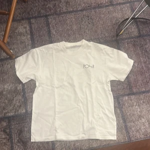 Vit t-shirt från Polar Skate Co. - Säljer en vit t-shirt från Polar Skate Co. med ett stilrent tryck på bröstet och ett stort, svart grafiskt tryck på ryggen. Perfekt för en avslappnad stil.