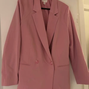 Rosa kavaj - Snygg rosa kavaj med knappar framtill. Perfekt för att liva upp garderoben med en färgklick. Kavajen har en klassisk design med långa ärmar och en stilren look.