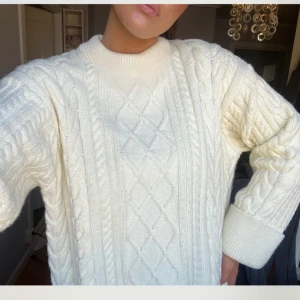 Vit stickad tröja - Säljer en mysig vit stickad tröja med kabelstickat mönster. Tröjan har långa ärmar och en rund halsringning. Perfekt för kyliga dagar!