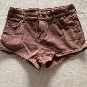 Bruna shorts från H&M Divided - Säljer ett par snygga bruna shorts från H&M Divided. De är tillverkade i bomull med en liten del elastan för extra komfort. Shortsen har en klassisk femficksdesign och knappstängning fram. Perfekta för varma sommardagar!