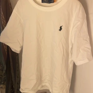 Vit t-shirt från Ralph Lauren - Säljer en klassisk vit t-shirt från Ralph Lauren med det ikoniska broderade logotypen på bröstet. T-shirten har en normal passform och är kortärmad, perfekt för en stilren och avslappnad look.