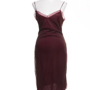 Vinröd klänning från Kookai - Elegant vinröd klänning från Kookai med smala axelband och en figurnära passform. Klänningen har en subtil v-ringning och är tillverkad i ett glansigt material som ger en lyxig känsla. Perfekt för speciella tillfällen.
