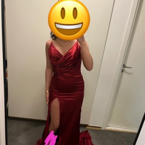 Vinröd långklänning med slits - Elegant vinröd långklänning med djup v-ringning och slits framtill. Klänningen är axelbandslös och har en figurnära passform som framhäver silhuetten. Perfekt för en festlig kväll eller bal.