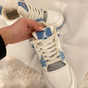 Nike Air Jordans i vitt och blått - Snygga Nike Air Jordans i vitt med ljusblå detaljer. Skorna har snörning och en ikonisk design med meshpaneler och den klassiska Jumpman-loggan på tungan och hälen. Perfekta för dig som vill ha en stilren och sportig look.