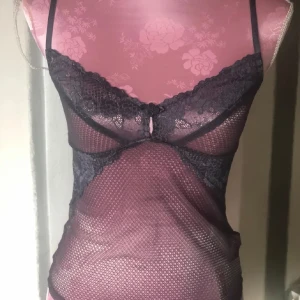 Grå  spetslinne - Elegant grå spetslinne med tunna axelband och vacker spetsdetalj över bysten. Materialet är genomskinligt och ger en sofistikerad look. Perfekt för att lägga till en touch av elegans till din outfit.