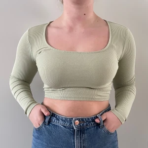 Grön ribbad croppad topp - Snygg grön ribbad croppad topp med långärmade ärmar. Perfekt för en trendig look. Toppen har en fyrkantig halsringning och är i en mjuk och stretchig kvalitet.