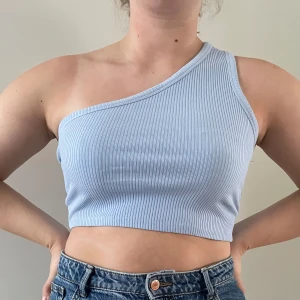 Ljusblå ribbad oneshoulder topp - Snygg ljusblå ribbad oneshoulder topp som är croppad och perfekt för sommardagar. Den har en stilren design och är lätt att matcha med olika outfits.