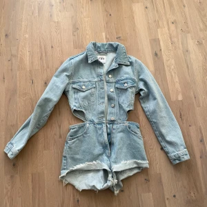 Ljusblå jeans playsuit från Zara - Trendig ljusblå jeans playsuit från Zara med långärmad jacka och shorts i ett. Den har en cool cut-out design i midjan och fransiga kanter på shortsen. Perfekt för en avslappnad stil med en twist.