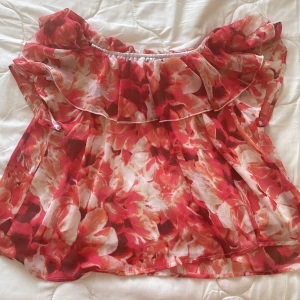 Blommig offshoulder topp från BikBok - Säljer en färgglad blommig offshoulder topp från BikBok. Toppen har volangdetaljer och är perfekt för sommarens varma dagar. Den har en luftig passform och är tillverkad i ett lätt material.