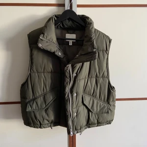 Dunväst - Olivgrön dunväst från H&M med dragkedja och knappar. Perfekt till vår/höst!