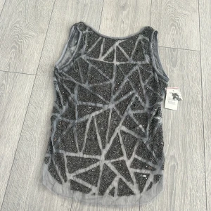 Grå glittrig linnetopp från ASOS  - Snygg grå linnetopp från ASOS med ett unikt geometriskt mönster av glittrande paljetter. Perfekt för att sticka ut på festen. Toppen är ärmlös och har en transparent look med ett coolt mönster. Toppen har en kortare rygg 
