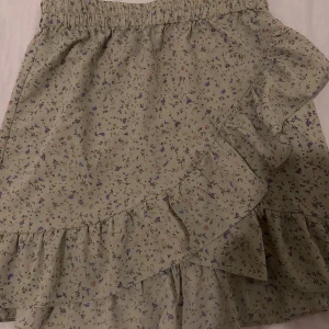 Blommig kjol med volang🤍 - Söt blommig kjol i ljusgrön nyans med små blommor i lila och brunt. Kjolen har en volangdetalj framtill och elastisk midja för en bekväm passform. Perfekt för vår och sommar!