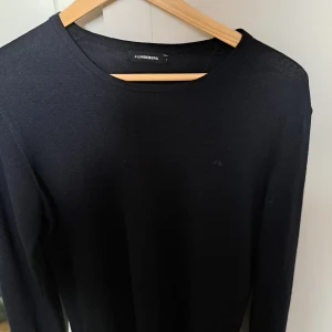 Tröja i merinoull från J.lindeberg  - Snygg och stilren svart långärmad tröja från J.Lindeberg. Perfekt för en minimalistisk look. Tröjan har en enkel design med rund hals och är tillverkad i ett mjukt material. Fint skick och endast använd ett fåtal gånger