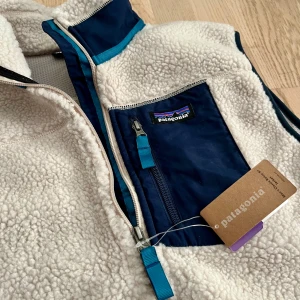 Patagonia väst - Men's Classic Retro-X® Fleece Vest - Säljer en helt ny och oanvänd, storlek L - Man, vit fleeceväst från Patagonia med blå detaljer. Västen har dragkedja framtill och en praktisk bröstficka med dragkedja.  🧗🏻‍♂️🏔️