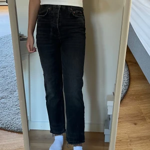 Svarta högmidjade jeans - Säljer ett par svarta högmidjade jeans med en klassisk femficksdesign. Jeansen har en rak passform och är perfekta för en stilren look. De är tillverkade i ett slitstarkt denimtyg och har en knappgylf.
