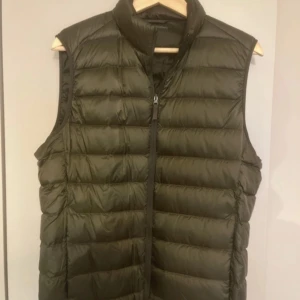 Olivgrön dunväst från Uniqlo - Säljer en olivgrön dunväst från Uniqlo Ultra Light Down. Västen har en hög krage, dragkedja framtill och är quiltad för extra värme. Perfekt för lager-på-lager och enkel att bära tack vare sin lätta vikt. Använd nån enstaka gång, som ny. Köpt för 499. 