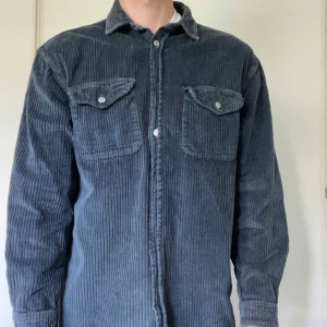 Grå manchesterskjorta från Zara - Säljer en grå manchesterskjorta från Zara med relaxed fit. Skjortan har långa ärmar, två bröstfickor med lock och knappar framtill. Perfekt för dig som gillar en lite mer avslappnad stil. Är mer likt en overshirt eller jacka robustare material 