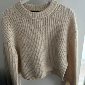 Beige stickad tröja - Mysig beige stickad tröja med grov ribbad struktur och rund halsringning. Tröjan har slits på slutet av ärmen och vid midjan (se bilder). Modellen är lite kortare an vanligt. Storlek xs❣️
