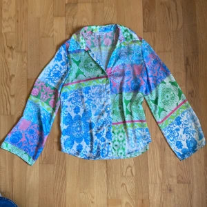 Färgglad mönstrad blus från Zara - Säljer en färgglad blus med lång ärm och krage. Skjortan har ett unikt mönster i blått, grönt, rosa och vitt med inslag av paisley och blommor. Knappar framtill och lätt, luftig känsla. 