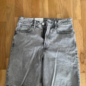 Grå jeansshorts från H&M - Säljer ett par grå jeansshorts från H&M med relaxed fit. Klassisk femficksmodell med knapp och dragkedja i gylfen. Perfekta till sommaren för en avslappnad stil. Storlek: W28, CN 170/72A