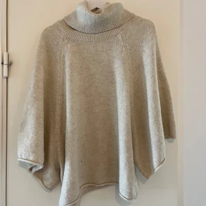 Beige stickad poncho med polokrage från Zara - Säljer en beige stickad poncho från Zara med hög polokrage. Ponchon har en lös och avslappnad passform och är perfekt för lager-på-lager under kyliga dagar. Mjuk och skön att bära.