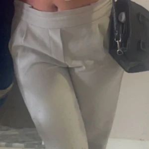 Beiga kostymbyxor med låg midja - Säljer ett par stilrena beiga kostymbyxor/ linnebyxor med låg midja och raka ben. Byxorna har en bred linning och klassisk passform, perfekta för en dressad look. Passar till många olika stilar och är lätta att matcha.