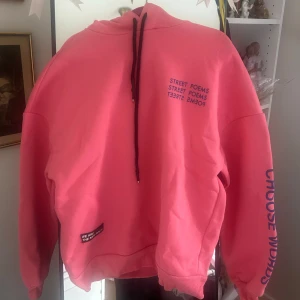 Rosa hoodie med coola tryck - Säljer en rosa hoodie från Pull & Bear med lila texttryck på bröstet och ärmen. Hoodien har huva med svarta snören och ribbade muddar. Köpt som dam XS, men är rätt så oversized så passar större storlekar samt män också. Använd typ en gång.