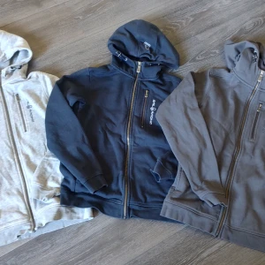 Hoodies från Sail Racing, 160. - 3 STYCK FÖR 500:- Ljusgrå, mörkblå och mörkgrå hoodies från Sail Racing med dragkedja framtill och bröstficka med dragkedja. Ljusgrå är välanvänd medan de andra två är i jättefint skick. Ljusgrå är även hel och ren, vad jag kan se.