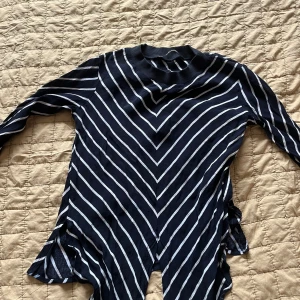 Svartvit randig tröja från Zara Basic - Säljer en svart tröja med vita diagonala ränder från Zara Basic. Tröjan har lång ärm, ribbad krage och sidoslitsar nertill. Perfekt för dig som gillar stilrena mönster och vill ha något bekvämt men snyggt.