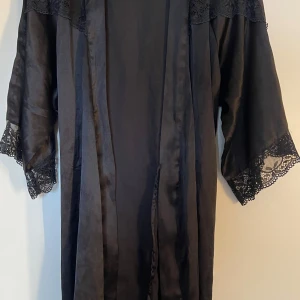 Svart kimono med spetsdetaljer från Pieces - Säljer en svart kimono från Pieces med vackra spetsdetaljer på ärmar och axlar. Kimonon har trekvartsärm och ett knytband i midjan. Perfekt att slänga på sig över något enkelt för en extra touch.