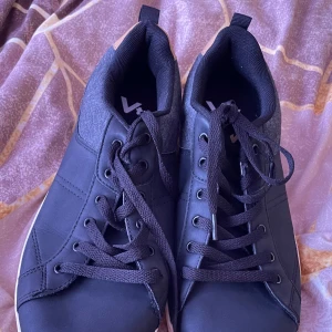 Svarta sneakers från Vty med beige detalj - Säljer ett par svarta sneakers från Vty med snygga beige detaljer på hälen och grå partier vid ankeln. Skorna har svarta snören, rund tå och vit platt sula. 