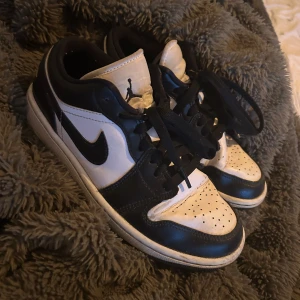 Nike Air Jordans svartvita sneakers - Svartvita Nike Air Jordans med klassisk låg modell och svart snörning. Skorna har vit tå med perforeringar, svart swoosh och detaljer samt Air Jordan-logga på hälen. Perfekta för dig som gillar streetwear och sportig stil.