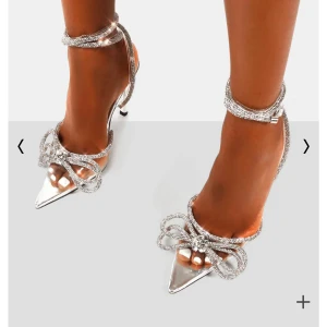 Silvriga klackar med rosett - Glittriga pumps i silver med spetsig tå, hög klack och dekorativa strassdetaljer. Skorna har en stor rosett framtill och smala remmar runt vristen. Aldrig använda och är i ny skick. Skriv för mer bilder🫶🏼