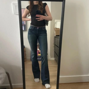 Mörkblå jeans från Rock & Republic - Snygga mörkblå jeans från Rock & Republic med broderade detaljer på bakfickorna. De har en bootcut-stil och är lågmidjade, vilket ger en trendig look. Perfekta för att ge din outfit en cool touch. 