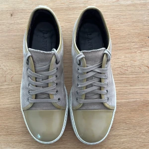 Beige sneakers från Lanvin med lackad tå - Säljer ett par snygga sneakers från Lanvin i beige mocka med matchande beige lackad tå och detaljer. Skorna har snörning och vit sula, perfekt för dig som gillar stilrena och exklusiva sneakers, perfekt till sommaren! (Kan gå ner i pris vid snabb affär)