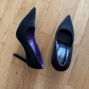 Svarta pumps med spetsig tå - Säljer ett par eleganta svarta pumps från Berskha med hög klack och spetsig tå. Skorna har en stilren design och insida i lila. Perfekta för dig som vill ha en klassisk och tidlös look.