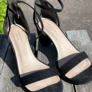 Klackar - Svarta klackar med ankelrem. Endast använda vid ett tillfälle. Klackhöjd ca 6,5 cm. Normala i storleken.