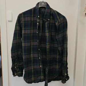 Rutig skjorta från Polo Ralph Lauren - Snygg långärmad skjorta i mörkblått och grönt rutigt mönster från Polo Ralph Lauren. Klassisk krage och knäppning framtill med vita knappar. Perfekt för dig som gillar en tidlös och avslappnad stil.