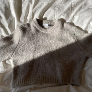Beige croppad stickad tröja från ZARA - Säljer en beige croppad stickad tröja från ZARA. Tröjan har rund halsringning och långa ärmar med ribbade muddar