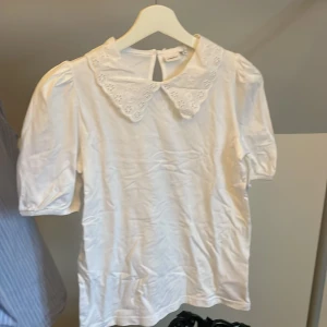 Vit blus med spetskrage från Name It - Säljer en söt vit blus från Name It med korta puffärmar och stor spetskrage med broderade blommor. Blusen har en knapp i nacken för enkel påklädning. Perfekt för dig som gillar romantisk stil! Ny utan prislapp💞