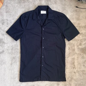 Marinblå skjorta Lindbergh - Säljer en marinblå skjorta från Lindbergh med korta ärmar och klassisk krage. Skjortan har knäppning framtill och är perfekt för en stilren look. Passar XS/S.