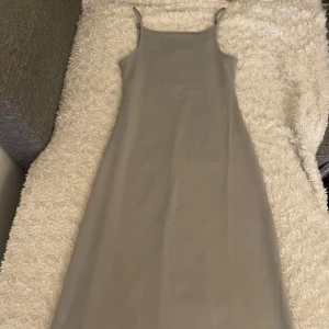 Grå tajt långklänning med smala axelband - En grå långklänning med smala axelband och tajt passform. 