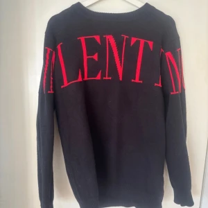 Svart tröja med röd VALENTINO-logga - Säljer en svart tröja från Valentino med stor röd logga över bröstet. Tröjan har rund halsringning och långa ärmar. Materialet är en blandning av viskos, nylon och polyester vilket gör den mjuk och bekväm.