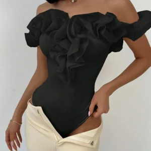 Svart offshoulder topp med volang - Säljer en svart offshoulder topp (body) med stora volangdetaljer framtill och runt axlarna. Toppen har en figurnära passform och är perfekt för att skapa en trendig look.