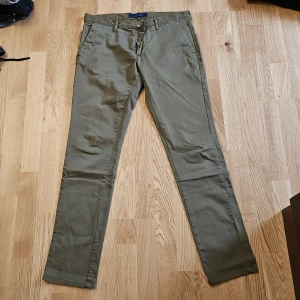 Olivgröna chinos Zara Man - Snygga olivgröna chinos med normal passform och raka ben. Klassisk design med fickor fram och bak samt hällor för bälte. Perfekta för en stilren och avslappnad look.