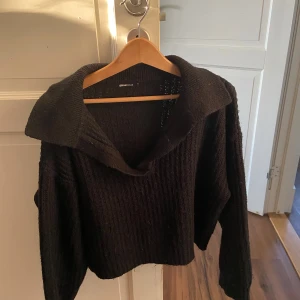 Svart stickad tröja från Gina Tricot - Säljer en svart stickad tröja från Gina Tricot. Tröjan har en bred krage och långa ärmar, perfekt för lager på lager. Ribbstickad struktur ger en snygg och trendig look.