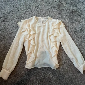 Vit blus med volangdetaljer - Säljer en stilren vacker vit blus med långa ärmar och volangdetaljer längs axlarna och framsidan. Storlek 36, men passar både S och M. Märke Carin Wester💖