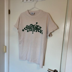 Beige t-shirt med grön Vintage Supply-tryck - Beige t-shirt från Vintage Supply med grönt retroinspirerat tryck framtill. Klassisk passform och rund halsringning. Sparsamt använd med ett litet diskret märke under första i:et.